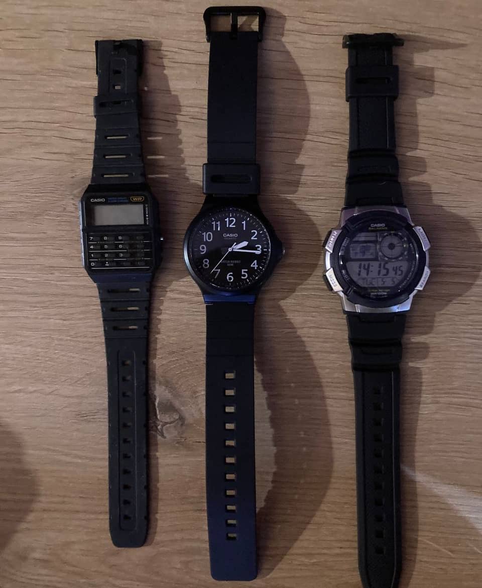 Three Casio watches on the table. On the right, a fancy CA-53W, a calculator watch, lies—no signs of life, no digits on the screen. In the middle, Casio MV-240 watch, with actual arrows and a dial! On the right, Casio AE-1000W, a relatively ugly watch with world map, artificial dial, timer, stopwatch, alarm, and everything. It looks extremely ugly though, even with sanded-down markings and black strap (the watch itself is navy blue.)